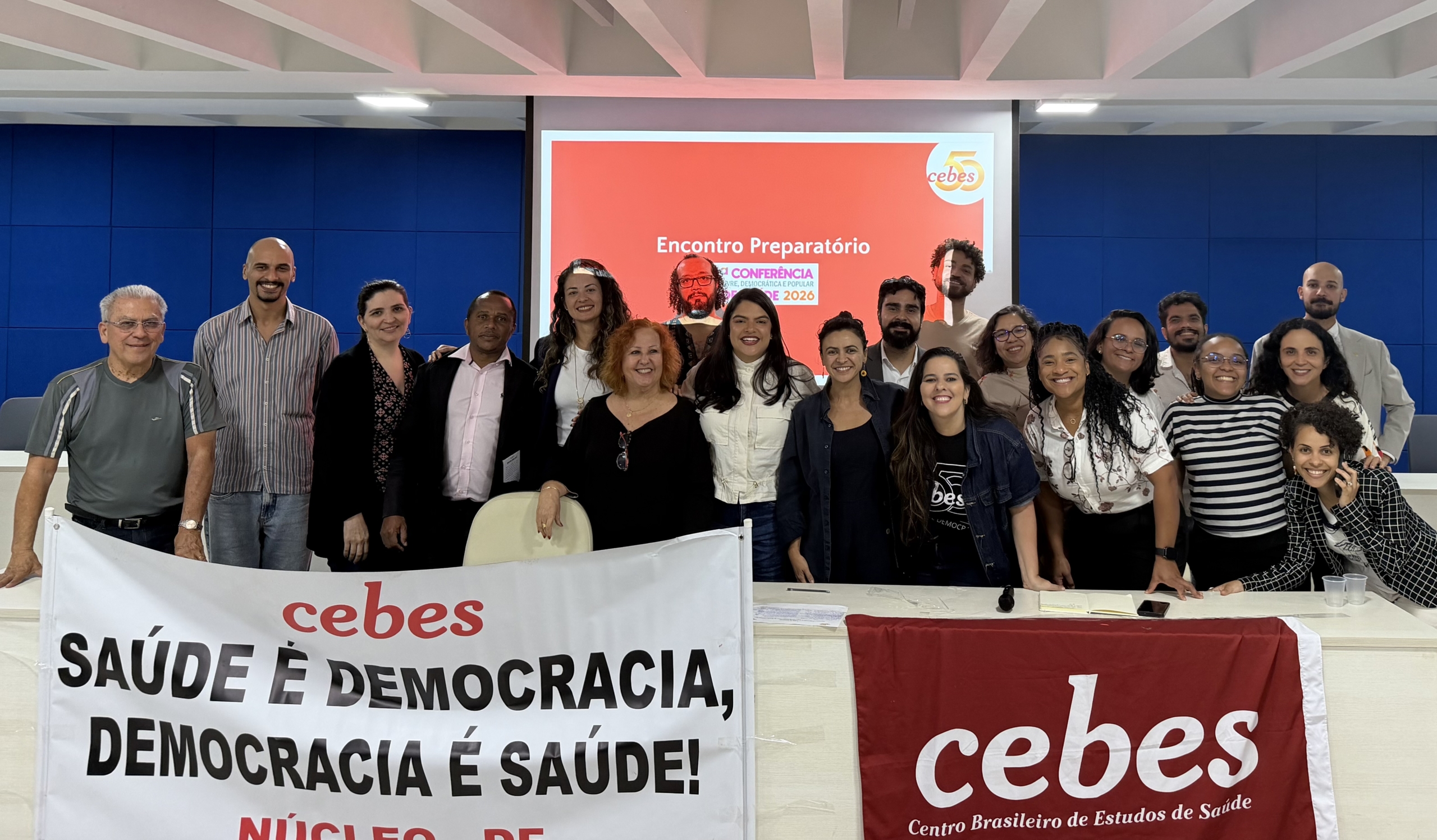 Pessoas de diversas reunidas com faixas em um auditório. Ao fundo, se lê: encontro preparatório