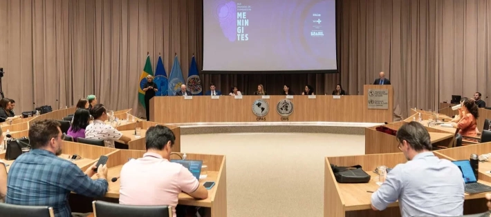 Uma sala de conferências ampla com várias pessoas sentadas ao redor de mesas retangulares