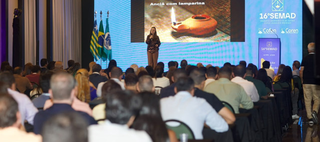 Uma mulher falando ao microfone em uma palestra para várias pessoas